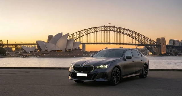 The OSPIPO sedan at the kerb outside a Sydney terminal, boot open, ready to load